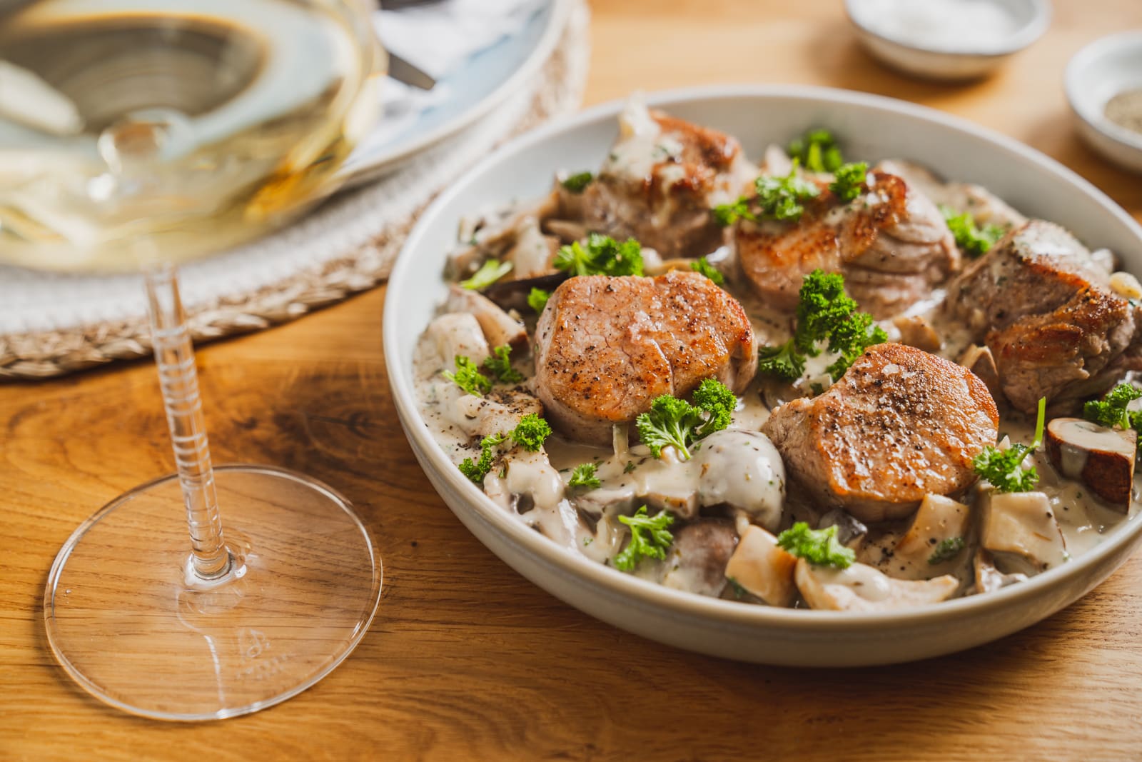 Schweinemedaillons in Champignonrahmsoße. Unser liebstes Sonntagsessen 1 Schweinemedaillons in Champignonrahmsoße in einer Schüssel, daneben ein Glas Riesling